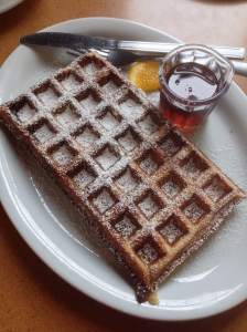 Waffle with powdered sugar and a side of maple syrup