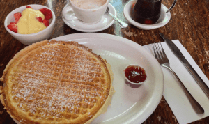 Waffle served with lemon curd, fresh strawberries, and strawberry jam, all with a side of maple syrup from Le Bateau Ivre