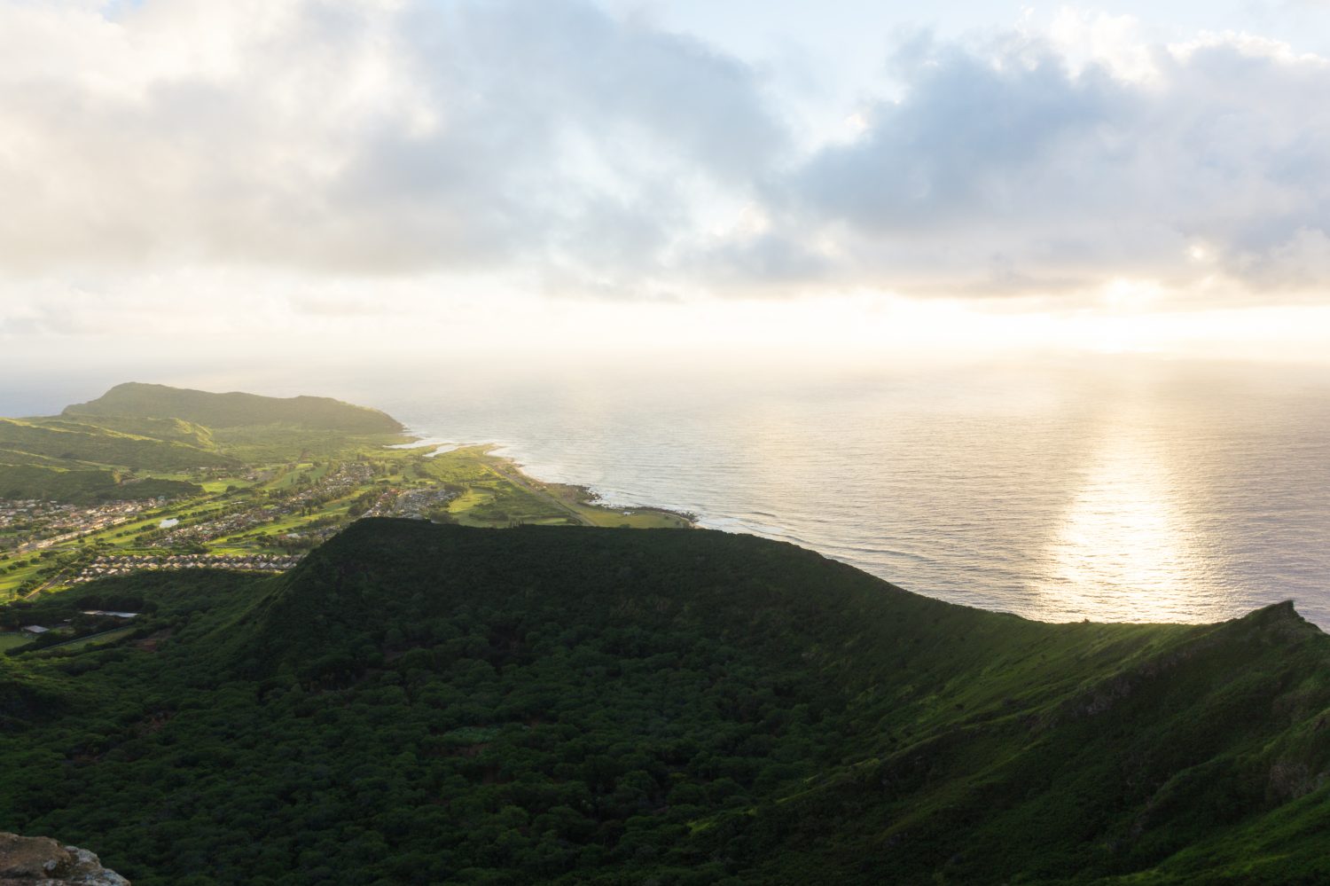 Sun shining down on green hills and a town in the distance, ocean in the background